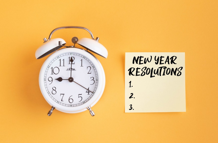 A white alarm clock next to a note reading New Year Resolutions 1. 2. 3.